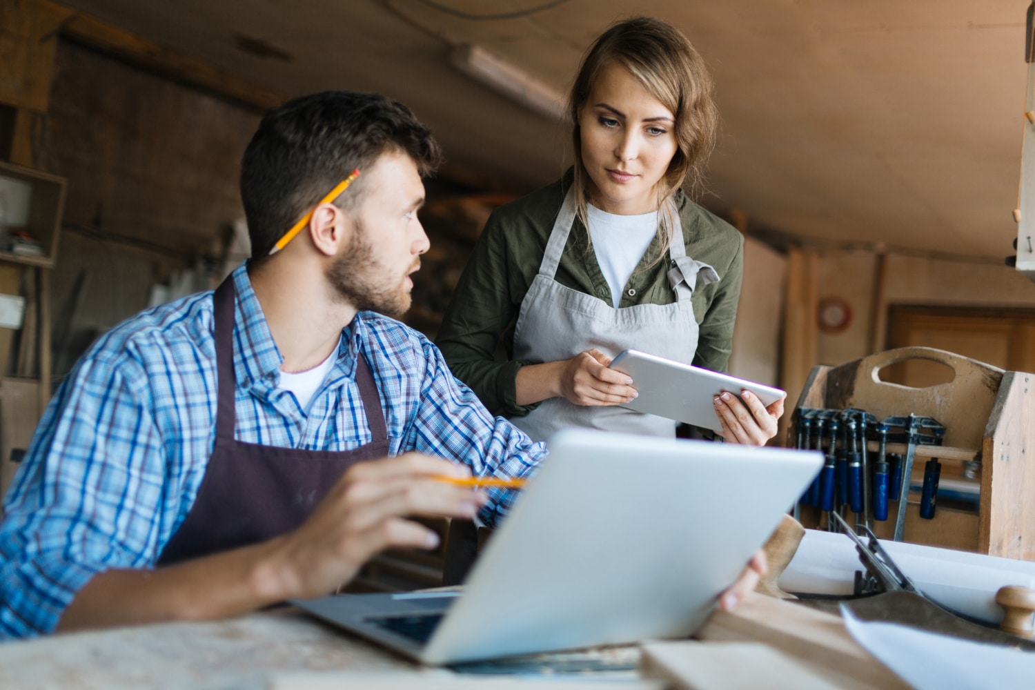 Two small business owners in a woodworking shop using digital solutions for small business owners, working with a laptop and tablet to manage their operations.